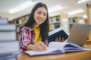 Female college student working on laptop and searching for books to study, make report, find useful information in college room. Concept of reading, learning and intelligence. photo