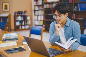 Male college students are working on laptops and searching for books to study, make reports, find useful information in college room. Concept of reading, learning and intelligence. photo
