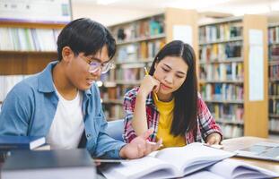 Students are consulting each other working on laptops and searching for books to study, make reports, find useful information in university room. Concept of reading, learning and intelligence. photo
