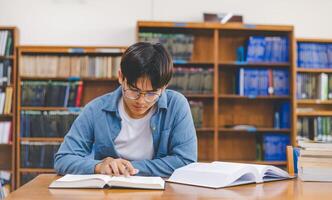 Male college students are working on laptops and searching for books to study, make reports, find useful information in college room. Concept of reading, learning and intelligence. photo
