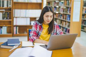 Female college student working on laptop and searching for books to study, make report, find useful information in college room. Concept of reading, learning and intelligence. photo