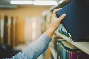 Close-up of hand picking up book on bookshelf in library to go to study.back to school concept photo