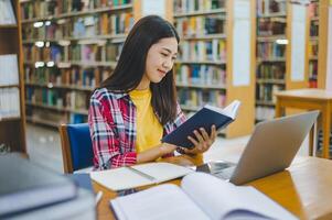 Female college student working on laptop and searching for books to study, make report, find useful information in college room. Concept of reading, learning and intelligence. photo