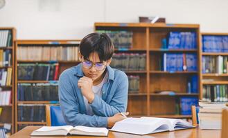 Male college students are working on laptops and searching for books to study, make reports, find useful information in college room. Concept of reading, learning and intelligence. photo