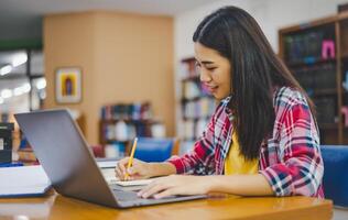 Female college student working on laptop and searching for books to study, make report, find useful information in college room. Concept of reading, learning and intelligence. photo