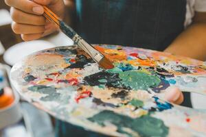 Close-up Art student's hand using a paintbrush to mix colors on a palette in hand to watercolor painting on canvas doing some art projects photo