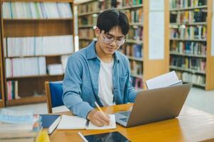 Male college students are working on laptops and searching for books to study, make reports, find useful information in college room. Concept of reading, learning and intelligence. photo