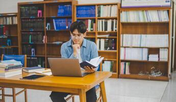 Male college students are working on laptops and searching for books to study, make reports, find useful information in college room. Concept of reading, learning and intelligence. photo