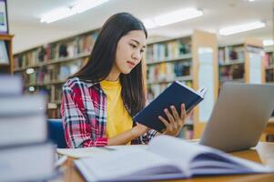 Female college student working on laptop and searching for books to study, make report, find useful information in college room. Concept of reading, learning and intelligence. photo