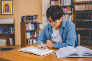Male college students are working on laptops and searching for books to study, make reports, find useful information in college room. Concept of reading, learning and intelligence. photo