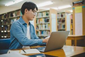 Male college students are working on laptops and searching for books to study, make reports, find useful information in college room. Concept of reading, learning and intelligence. photo