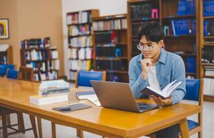 Male college students are working on laptops and searching for books to study, make reports, find useful information in college room. Concept of reading, learning and intelligence. photo