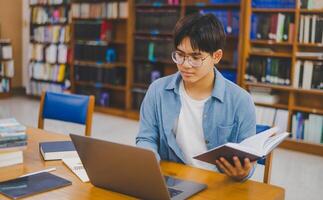 Male college students are working on laptops and searching for books to study, make reports, find useful information in college room. Concept of reading, learning and intelligence. photo