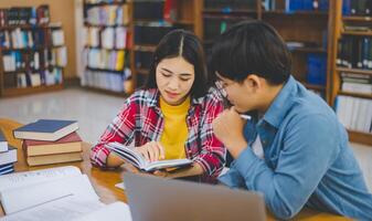Students are consulting each other working on laptops and searching for books to study, make reports, find useful information in university room. Concept of reading, learning and intelligence. photo