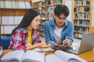 Students are consulting each other working on laptops and searching for books to study, make reports, find useful information in university room. Concept of reading, learning and intelligence. photo