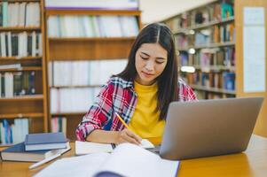 Female college student working on laptop and searching for books to study, make report, find useful information in college room. Concept of reading, learning and intelligence. photo