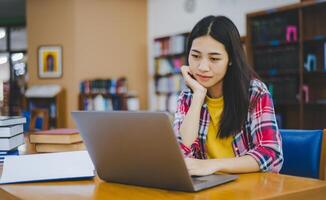 Female college student working on laptop and searching for books to study, make report, find useful information in college room. Concept of reading, learning and intelligence. photo