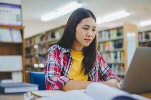 Female college student working on laptop and searching for books to study, make report, find useful information in college room. Concept of reading, learning and intelligence. photo