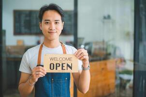 Smiling Asian coffee shop owner standing in front of cashier counter.welcome customers who come in to place orders in the cafe. photo