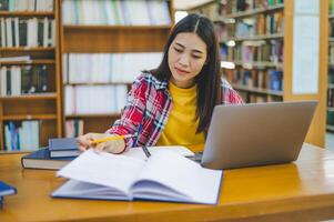 Female college student working on laptop and searching for books to study, make report, find useful information in college room. Concept of reading, learning and intelligence. photo