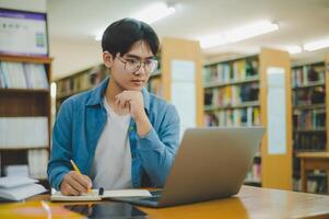 Male college students are working on laptops and searching for books to study, make reports, find useful information in college room. Concept of reading, learning and intelligence. photo