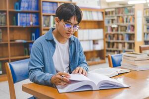 Male college students are working on laptops and searching for books to study, make reports, find useful information in college room. Concept of reading, learning and intelligence. photo