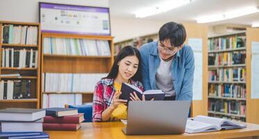 Students are consulting each other working on laptops and searching for books to study, make reports, find useful information in university room. Concept of reading, learning and intelligence. photo
