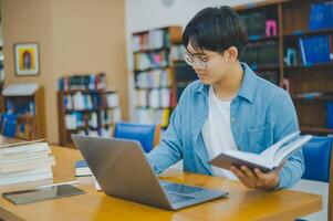 Male college students are working on laptops and searching for books to study, make reports, find useful information in college room. Concept of reading, learning and intelligence. photo