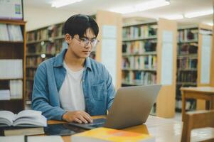 Male college students are working on laptops and searching for books to study, make reports, find useful information in college room. Concept of reading, learning and intelligence. photo