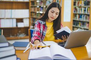 Female college student working on laptop and searching for books to study, make report, find useful information in college room. Concept of reading, learning and intelligence. photo