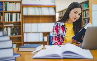 Female college student working on laptop and searching for books to study, make report, find useful information in college room. Concept of reading, learning and intelligence. photo