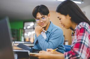 Students are consulting each other working on laptops and searching for books to study, make reports, find useful information in university room. Concept of reading, learning and intelligence. photo