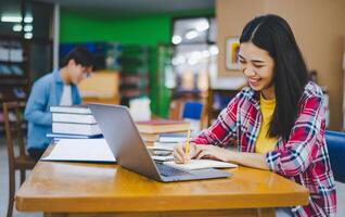 Female college student working on laptop and searching for books to study, make report, find useful information in college room. Concept of reading, learning and intelligence. photo