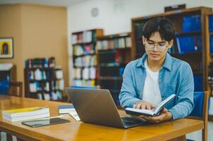 Male college students are working on laptops and searching for books to study, make reports, find useful information in college room. Concept of reading, learning and intelligence. photo