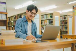 Male college students are working on laptops and searching for books to study, make reports, find useful information in college room. Concept of reading, learning and intelligence. photo