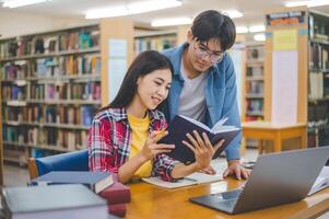 Students are consulting each other working on laptops and searching for books to study, make reports, find useful information in university room. Concept of reading, learning and intelligence. photo