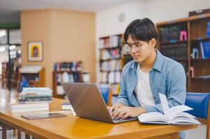 Male college students are working on laptops and searching for books to study, make reports, find useful information in college room. Concept of reading, learning and intelligence. photo