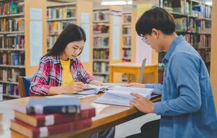 Students are consulting each other working on laptops and searching for books to study, make reports, find useful information in university room. Concept of reading, learning and intelligence. photo