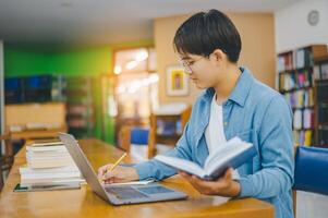 Male college students are working on laptops and searching for books to study, make reports, find useful information in college room. Concept of reading, learning and intelligence. photo