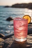 A glass of pink drink is on a rock by the ocean. photo