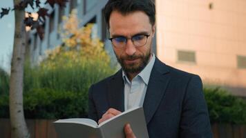 Thoughtful pensive man Caucasian businessman business coach in city write notes in notebook university professor writer thinking writing ideas at paper notepad smiling prepare for class lesson outside photo