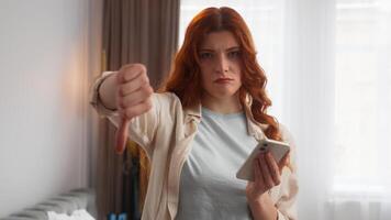 Caucasian woman girl checking sms type mobile phone smartphone app disagree unhappy emotion. Dissatisfied female showing thumb down in camera disapprove dislike sign no gesture home negative reaction photo