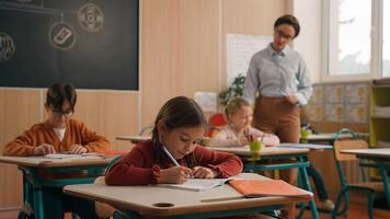 colegio clase lección niños estudiando aprendizaje en salón de clases mujer profesor hembra tutor caminando enseñando pequeño chico niño niño subir mano pedir ayuda pregunta responder estudiar aprender escribir hablando educación foto