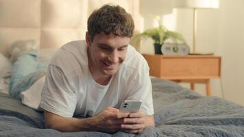 Caucasian man using mobile phone smartphone cellphone technology texting online chat smiling enjoying guy male bedroom home bed satisfied gadget connection communicate laughing happy messaging network photo