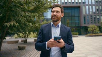 Caucasian middle-aged positive businessman in city male entrepreneur employer man business browsing chatting smartphone web distant communication connection looking away message with mobile phone photo