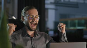 Caucasian emotional ecstatic excited businessman trader salesman business man employer office worker winner at night evening workplace win laptop online good result financial growth achieve success photo