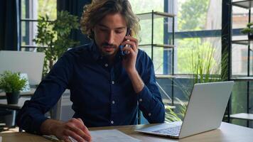 Arabian man hispanic businessman manager employer talk mobile phone search information on laptop check documents on desktop consulting client remote business consultation multitasking work in office photo