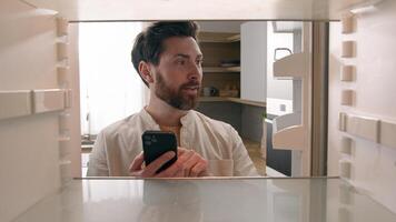 Hungry man guy open empty refrigerator poor crisis order food delivery with smartphone online buying products ordering goods with mobile phone store cellphone app point of view POV from inside fridge photo