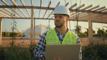 Thoughtful Caucasian male man experienced worker inspector helmet hardhat guy engineer technician typing laptop computer entering data internet pc analyzing project working blueprint construction park photo