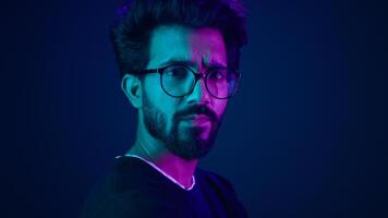 Close up male portrait in neon ultraviolet blue background Indian man Muslim Arabian guy posing in profile turning head looking at camera with serious face expression hacker developer coding worker photo